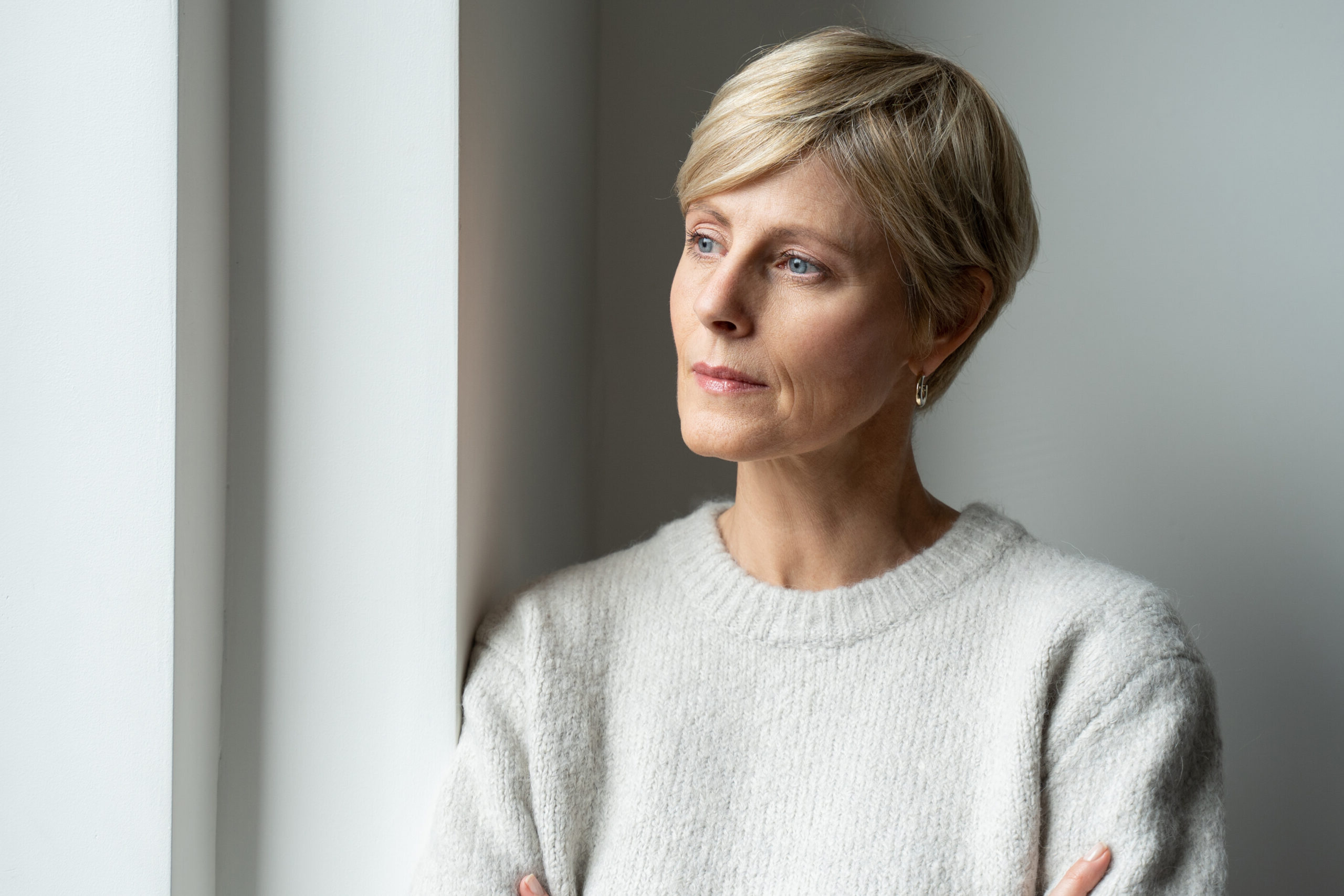 A thoughtful middle-aged woman looks out the window and is sad