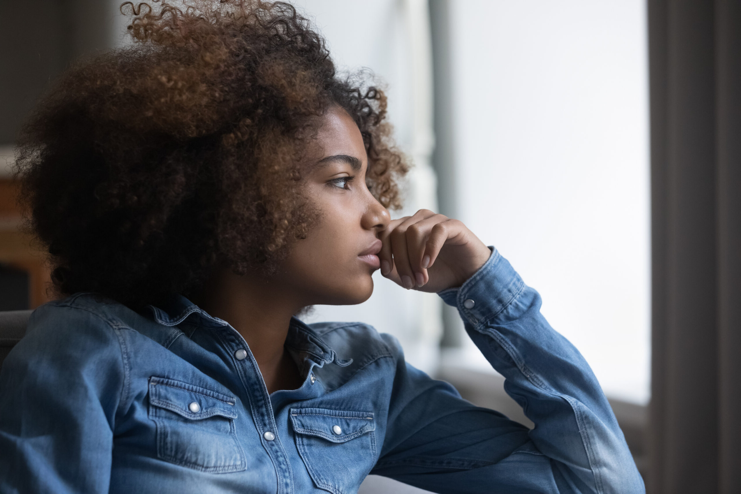 teenager black woman looking out of a window solemnly