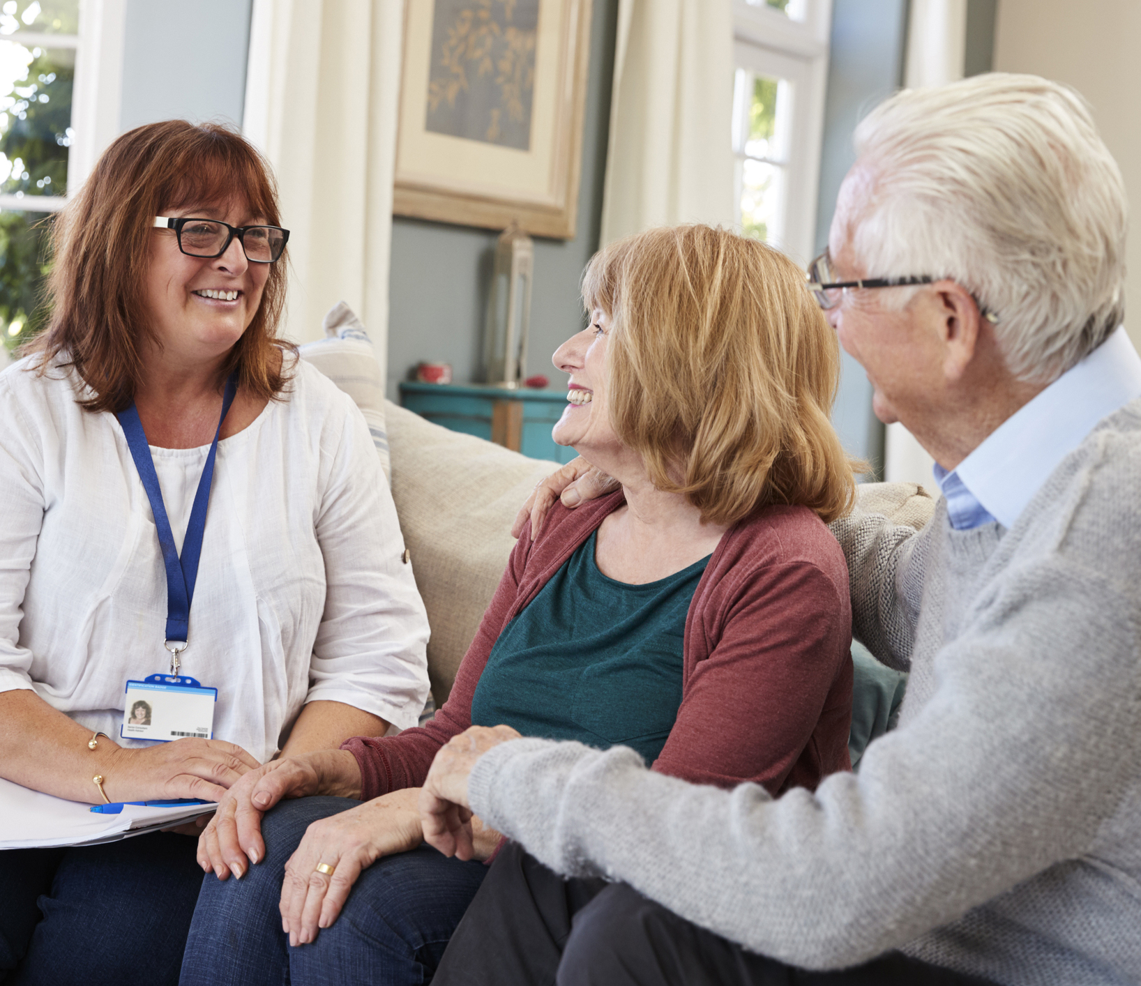 Support worker smiling, sitting on a sofa talking to a couple